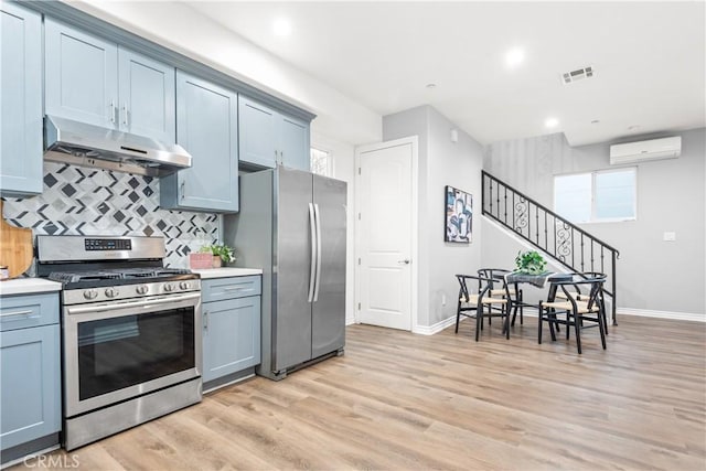 kitchen featuring light wood finished floors, light countertops, under cabinet range hood, a wall mounted air conditioner, and appliances with stainless steel finishes