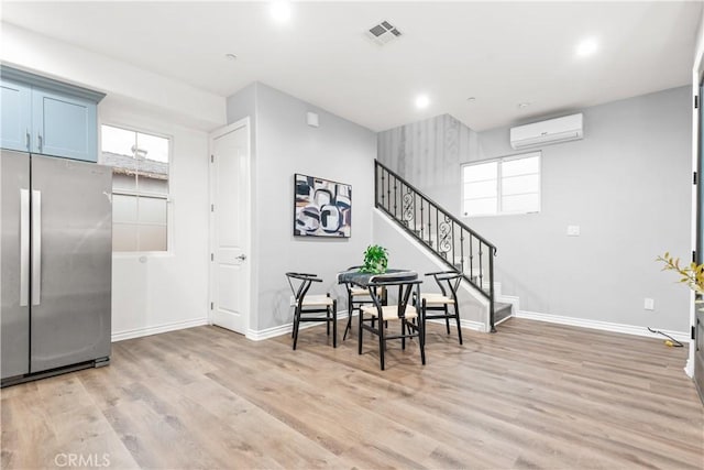 interior space featuring visible vents, baseboards, stairs, light wood-style floors, and a wall mounted air conditioner