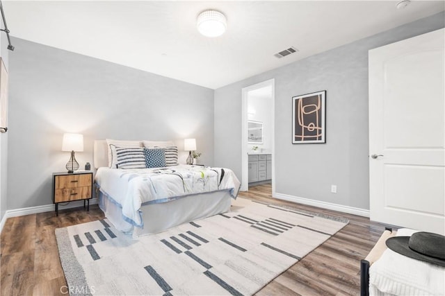 bedroom with visible vents, ensuite bathroom, baseboards, and wood finished floors