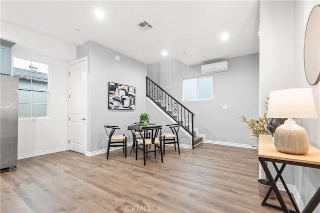 dining space with stairway, visible vents, baseboards, light wood-style floors, and a wall mounted air conditioner