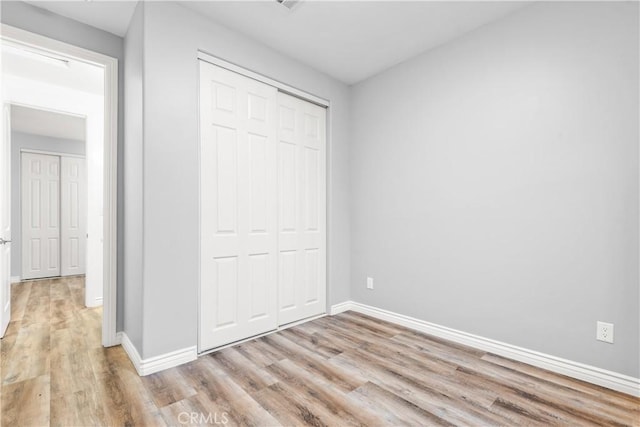 unfurnished bedroom with light wood-type flooring, baseboards, and a closet