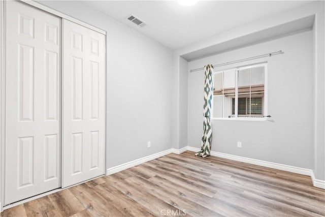 unfurnished bedroom with visible vents, baseboards, a closet, and wood finished floors