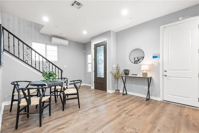 entrance foyer featuring baseboards, visible vents, light wood finished floors, a wall mounted AC, and stairs