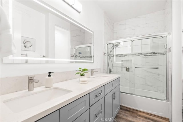 full bath with a sink, enclosed tub / shower combo, wood finished floors, and double vanity