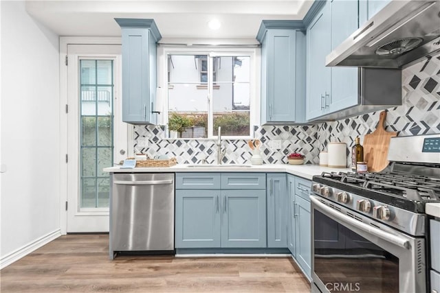 kitchen with blue cabinets, under cabinet range hood, a sink, appliances with stainless steel finishes, and light countertops