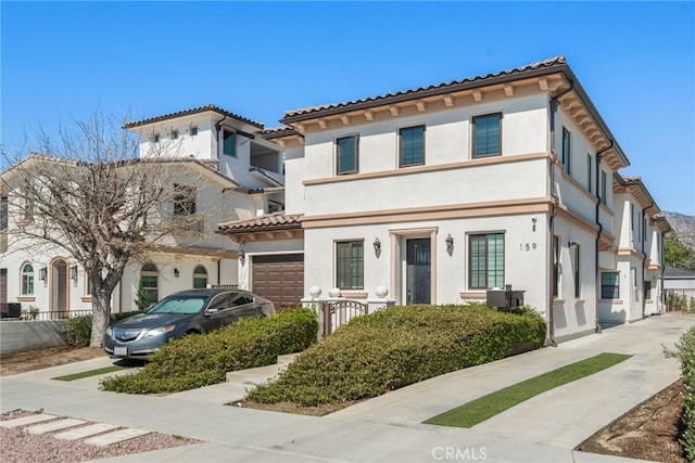 mediterranean / spanish home featuring stucco siding, a garage, a tile roof, and fence