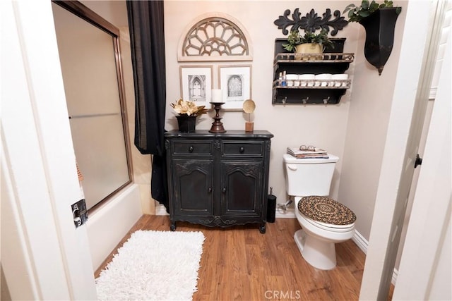 bathroom featuring bath / shower combo with glass door, wood finished floors, toilet, and baseboards