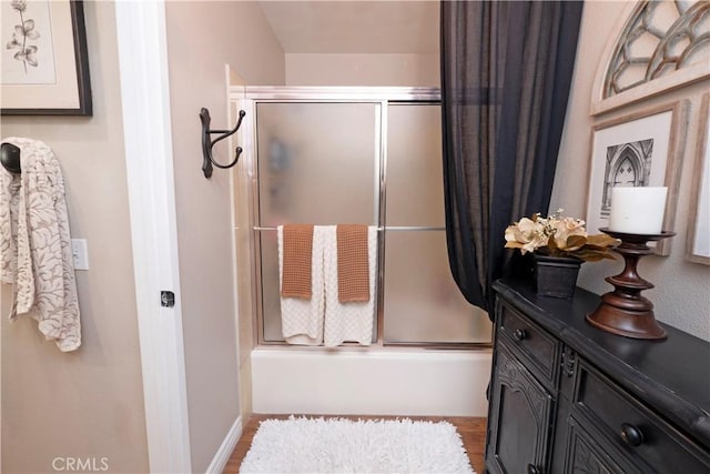 bathroom with wood finished floors, vanity, baseboards, and bath / shower combo with glass door