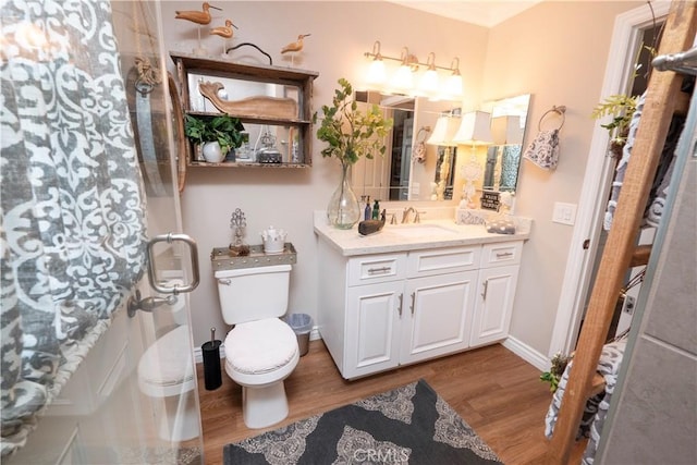 bathroom with toilet, wood finished floors, vanity, baseboards, and a shower