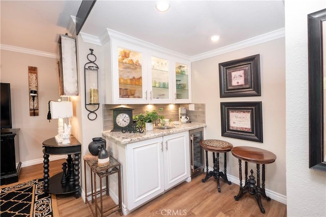 bar featuring beverage cooler, baseboards, decorative backsplash, crown molding, and light wood-style floors