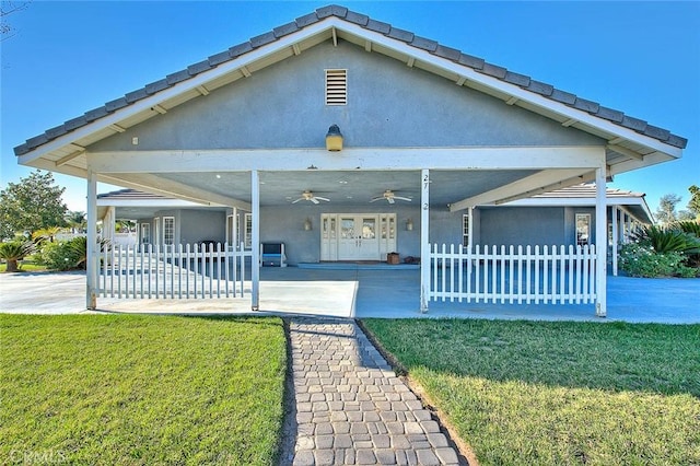 view of front of property featuring fence, a ceiling fan, french doors, stucco siding, and a front lawn