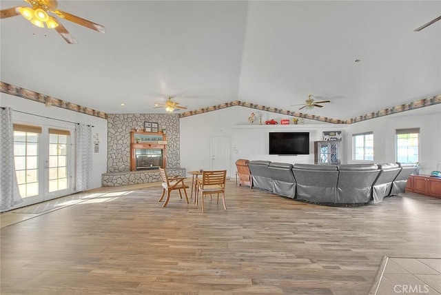 living area with ceiling fan, light wood finished floors, vaulted ceiling, and a fireplace