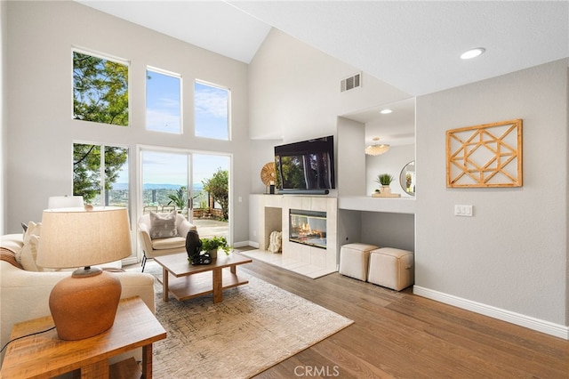 living area with a tile fireplace, visible vents, baseboards, and wood finished floors