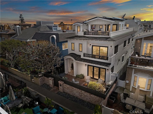 back of property at dusk with a fenced backyard and a balcony