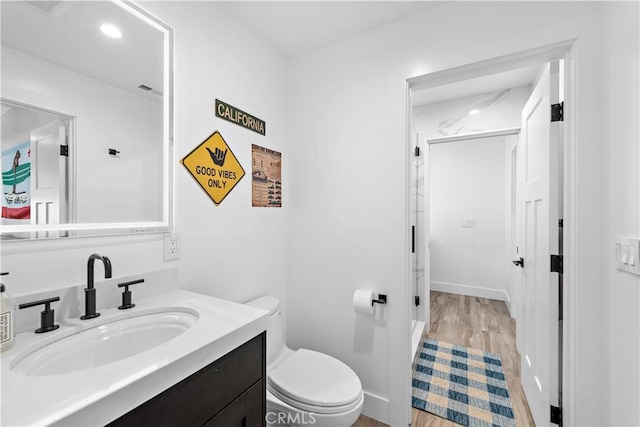 bathroom with baseboards, toilet, wood finished floors, vanity, and recessed lighting