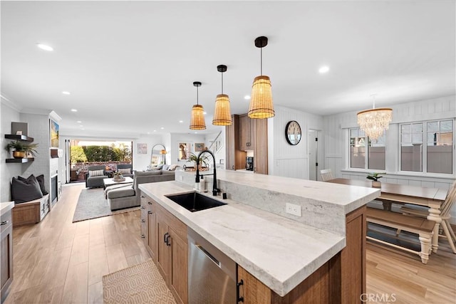 kitchen featuring stainless steel dishwasher, a kitchen island with sink, light wood-style floors, and a sink