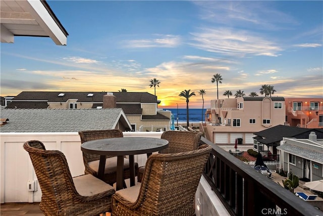 balcony at dusk featuring outdoor dining area and a water view