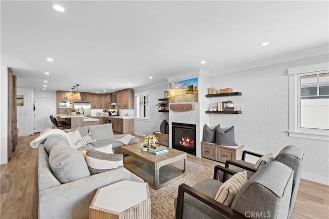 living room featuring recessed lighting, brick wall, light wood finished floors, a glass covered fireplace, and crown molding