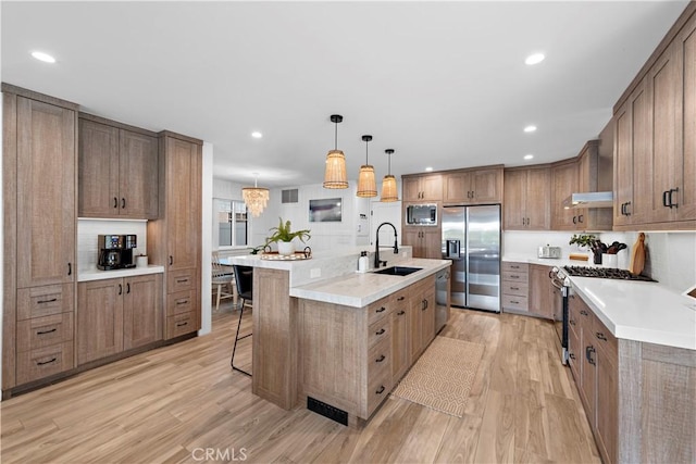 kitchen with appliances with stainless steel finishes, a sink, light wood finished floors, and a kitchen breakfast bar