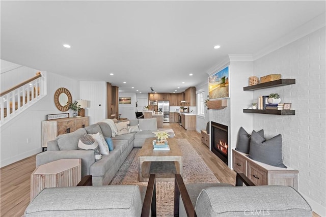 living area with recessed lighting, a large fireplace, brick wall, stairs, and light wood finished floors