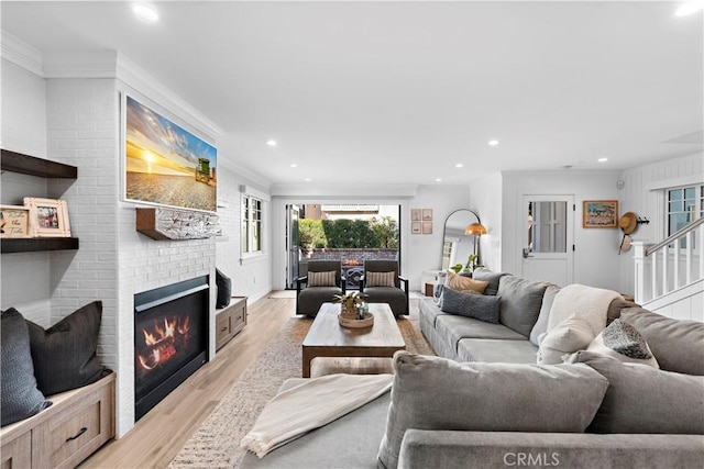 living room featuring light wood-style flooring, stairway, ornamental molding, a brick fireplace, and recessed lighting