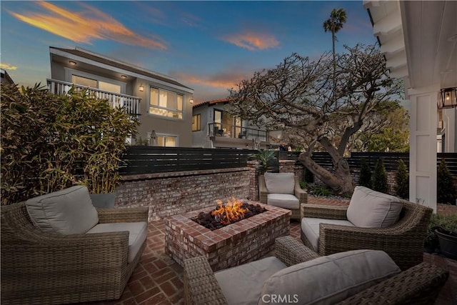 patio terrace at dusk with an outdoor living space with a fire pit, fence, and a balcony