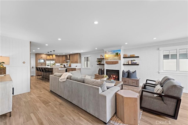 living area with light wood-type flooring, a fireplace, crown molding, and recessed lighting