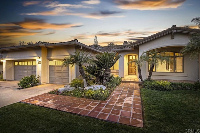 view of front facade featuring an attached garage, a tile roof, driveway, stucco siding, and a front yard