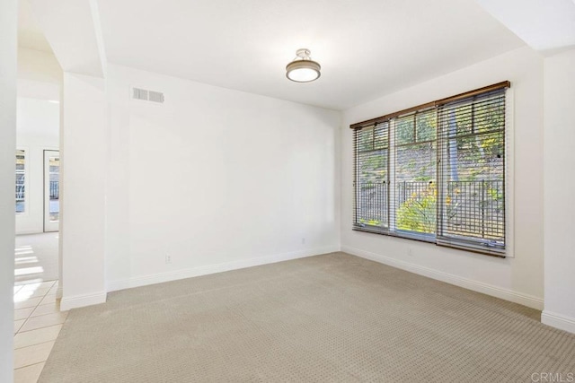 empty room with light colored carpet, visible vents, baseboards, and light tile patterned floors