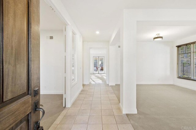 hall featuring light tile patterned floors, visible vents, baseboards, and light colored carpet