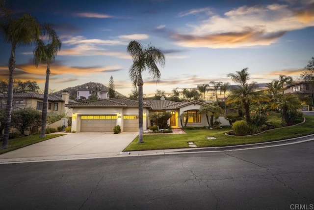 mediterranean / spanish-style house featuring an attached garage, driveway, a tiled roof, stucco siding, and a front yard