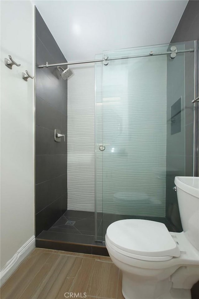 bathroom with wood finished floors, a shower stall, and toilet