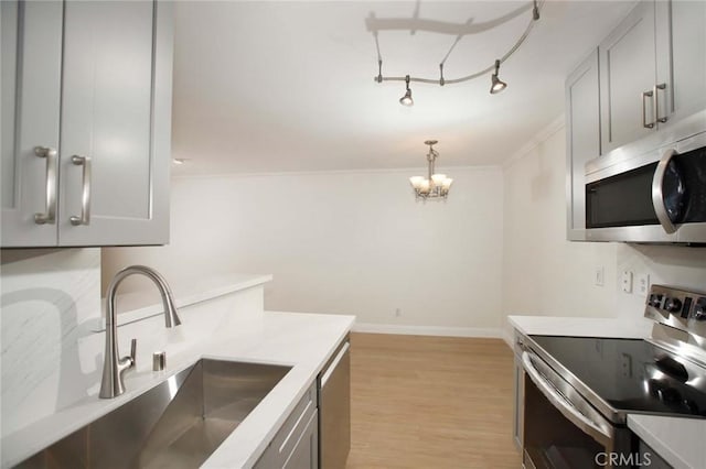 kitchen featuring a sink, baseboards, light wood-style floors, light countertops, and appliances with stainless steel finishes