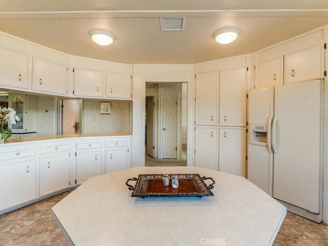 kitchen with light countertops, white refrigerator with ice dispenser, white cabinets, and visible vents