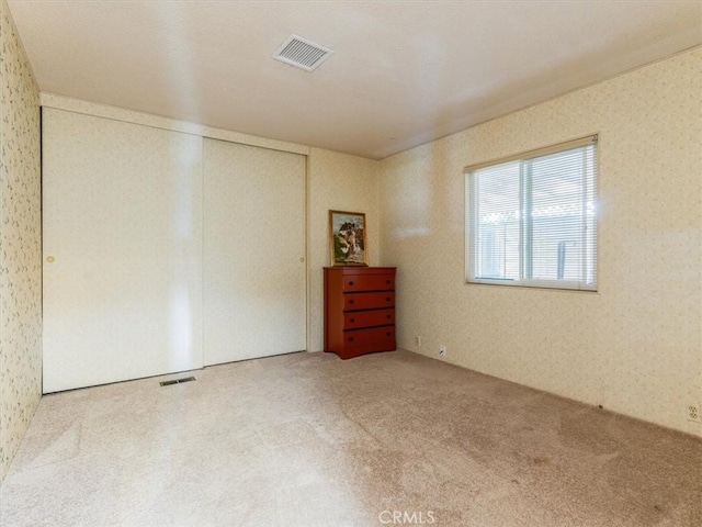 carpeted spare room with visible vents and wallpapered walls