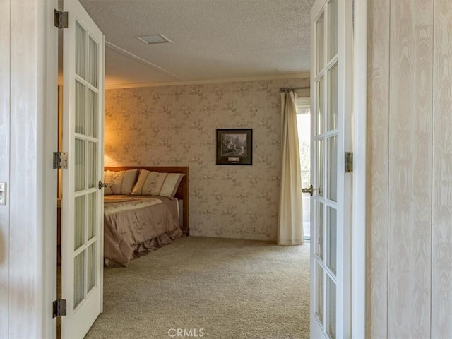 carpeted bedroom with a textured ceiling, french doors, ornamental molding, and wallpapered walls