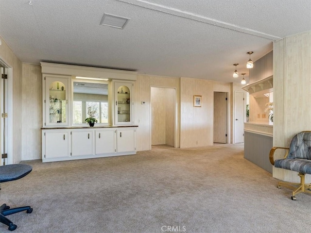 sitting room with light carpet, wood walls, a textured ceiling, and visible vents