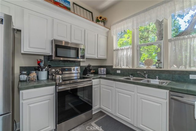 kitchen featuring stainless steel appliances, a sink, tile counters, and white cabinetry