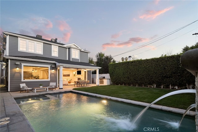 back of house at dusk featuring a pool with connected hot tub, a yard, and a patio