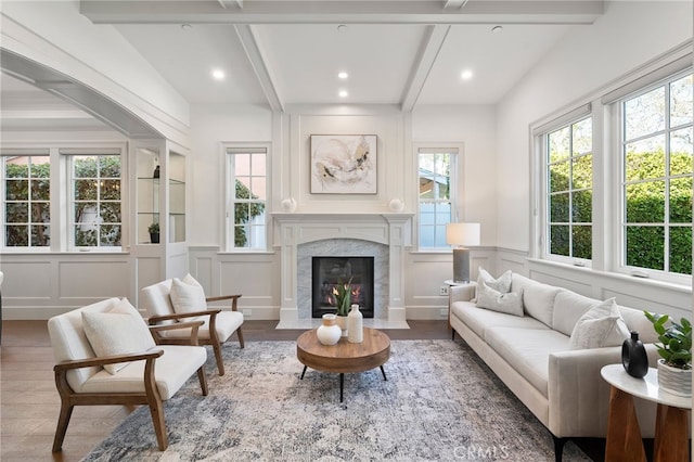 sitting room featuring a healthy amount of sunlight, wood finished floors, beamed ceiling, and a high end fireplace