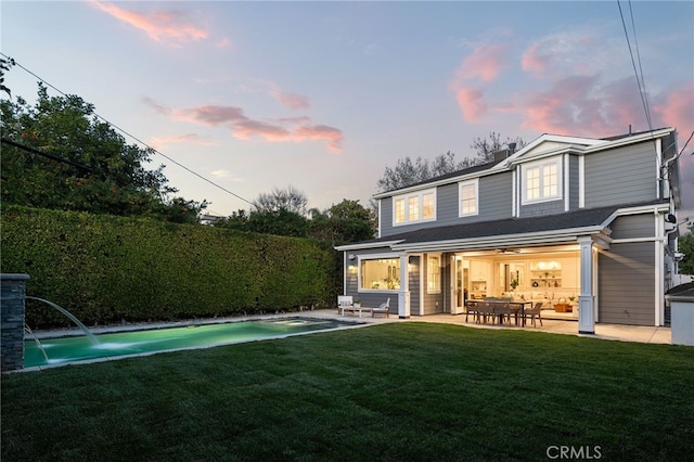 back of property at dusk featuring a lawn, a patio area, and a fenced in pool