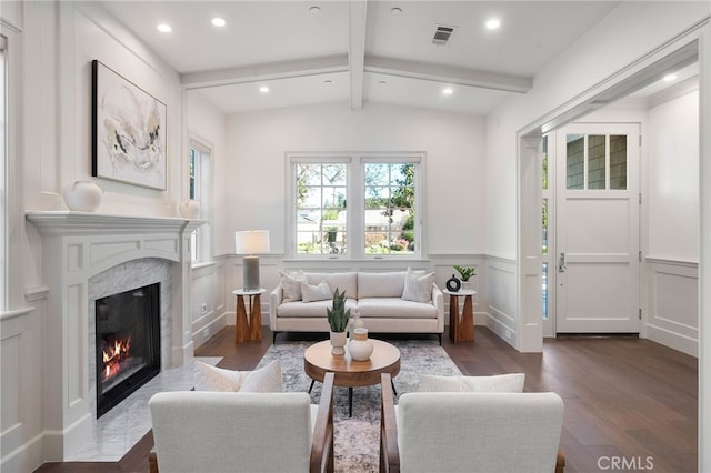 sitting room with dark wood finished floors, visible vents, a decorative wall, lofted ceiling with beams, and a high end fireplace