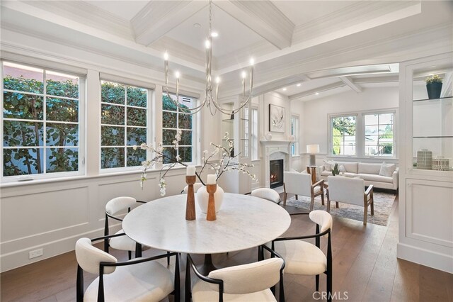 dining area with a warm lit fireplace, dark wood-type flooring, crown molding, and a decorative wall