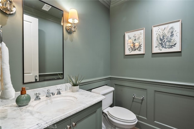 bathroom with toilet, a wainscoted wall, ornamental molding, vanity, and a decorative wall