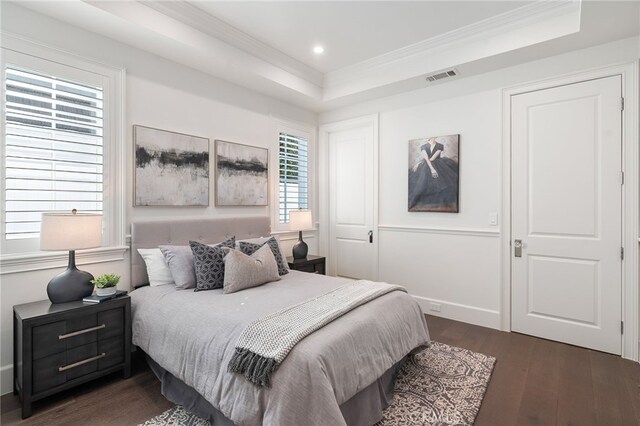 bedroom with a tray ceiling, ornamental molding, dark wood finished floors, and visible vents