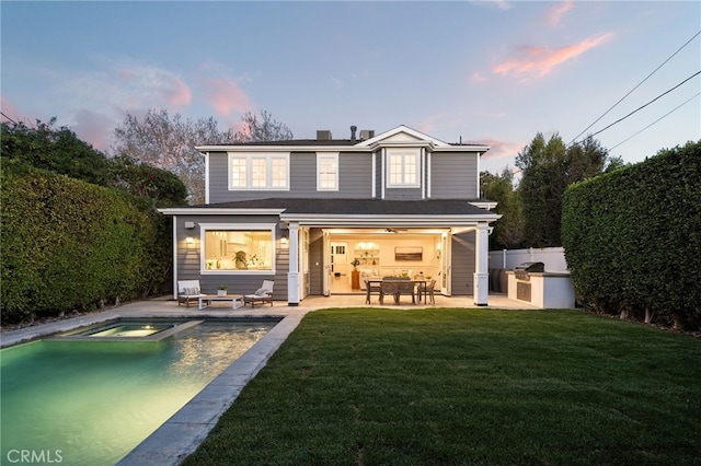 back of property at dusk featuring a pool with connected hot tub, a patio area, a yard, and fence