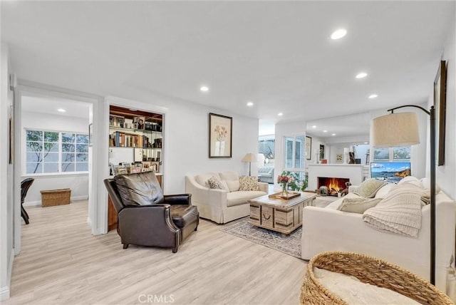 living room with light wood-style floors, recessed lighting, a lit fireplace, and baseboards