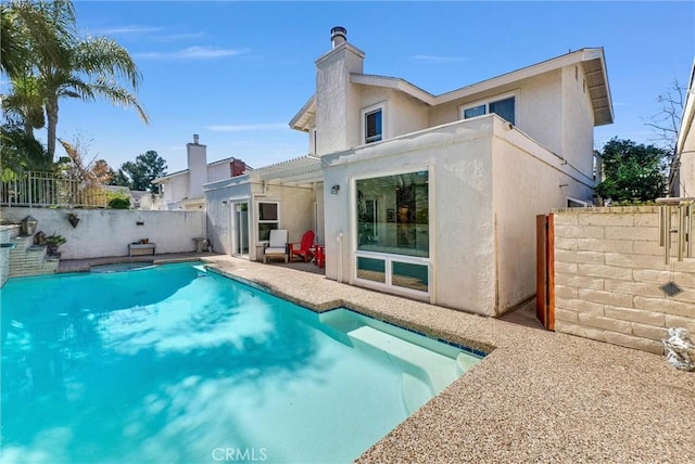 back of property with a fenced in pool, a chimney, stucco siding, a balcony, and a fenced backyard