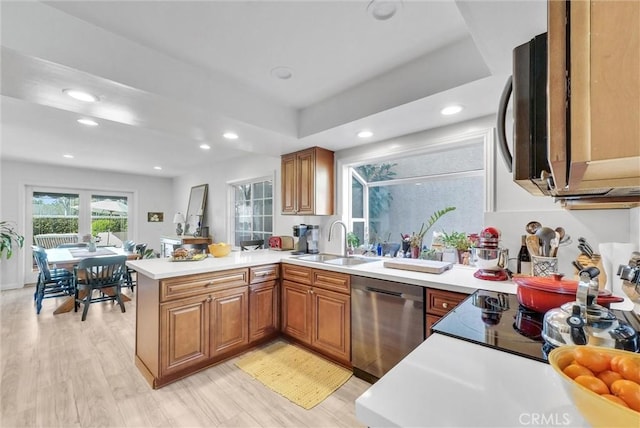 kitchen with a peninsula, a sink, light countertops, stainless steel dishwasher, and light wood-type flooring