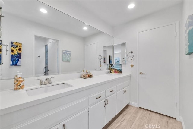 bathroom with recessed lighting, double vanity, a sink, and wood finished floors